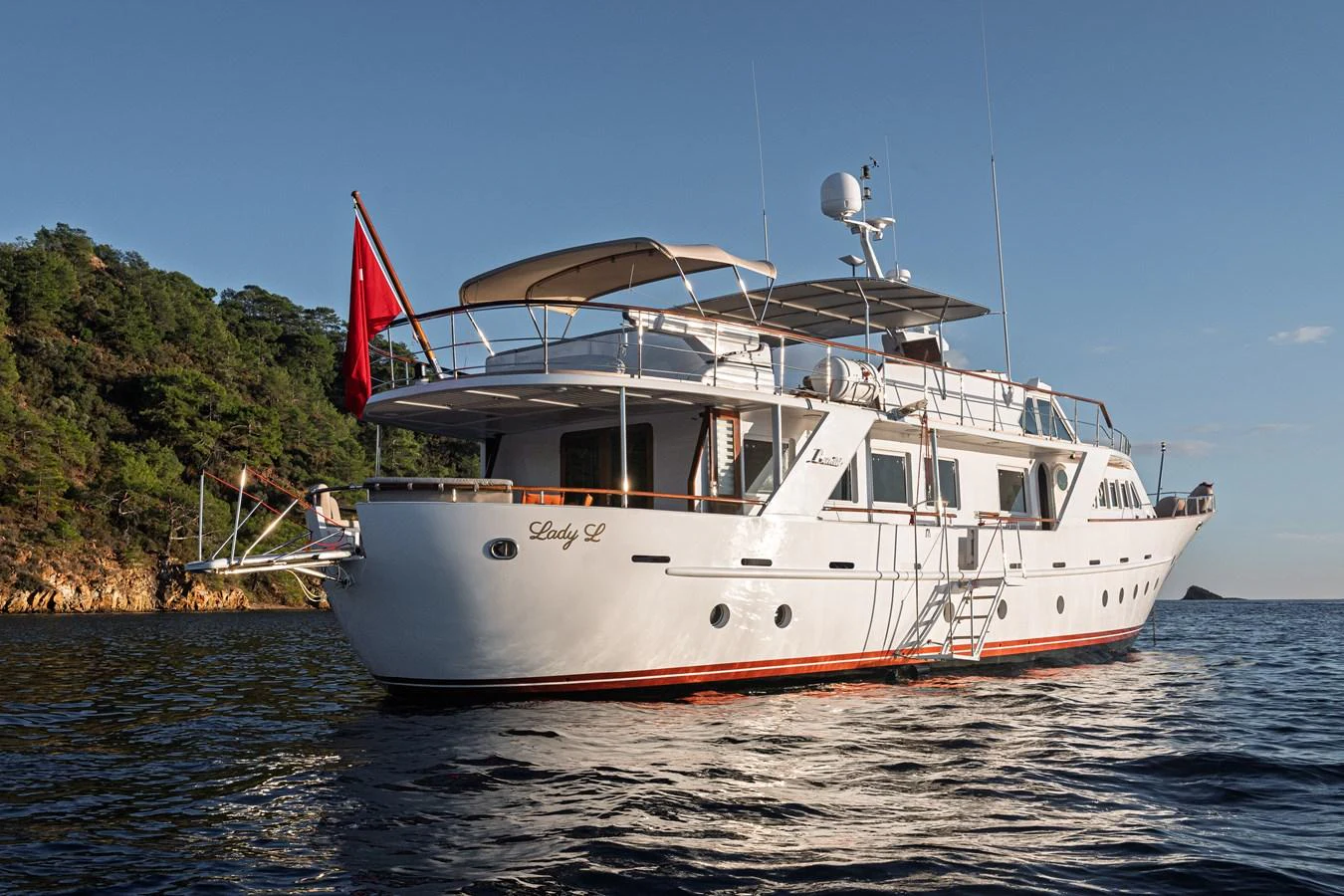 A classic yacht with elegant lines is anchored near a scenic coastline. aboard LADY L Yacht for Sale