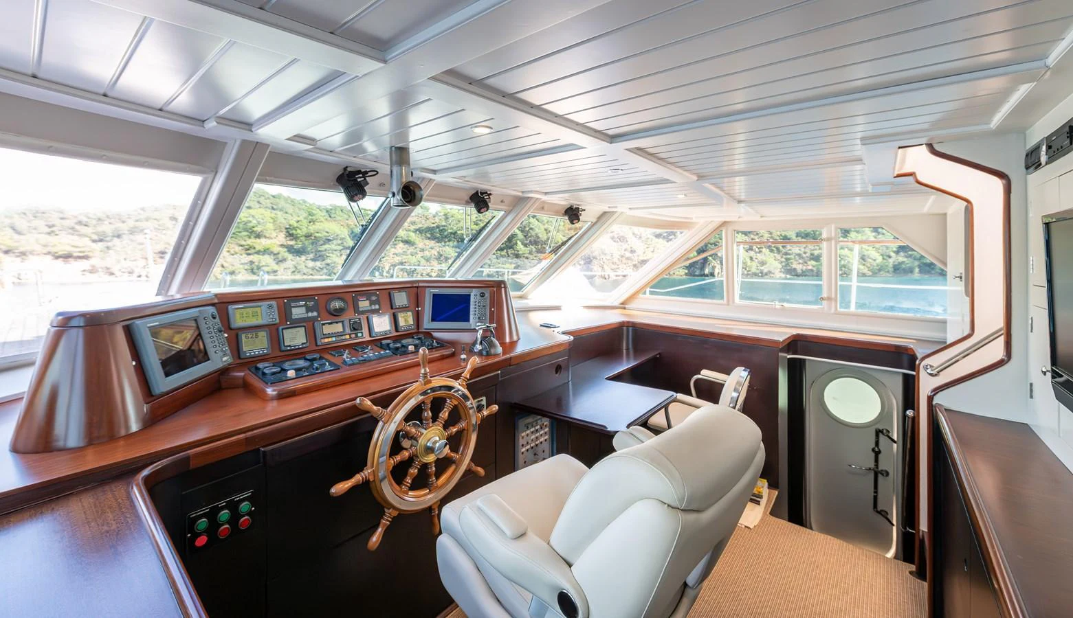The helm station features a classic wooden steering wheel and modern navigation equipment, offering panoramic views through large windows. aboard LADY L Yacht for Sale