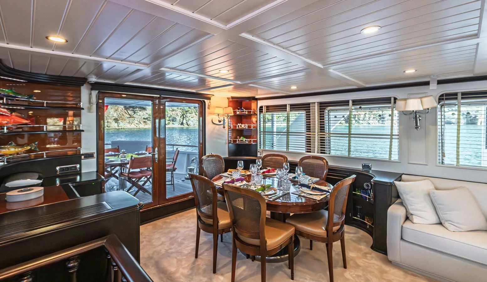 The yacht's dining area features a round table set for a meal, with large windows providing a scenic view. aboard LADY L Yacht for Sale