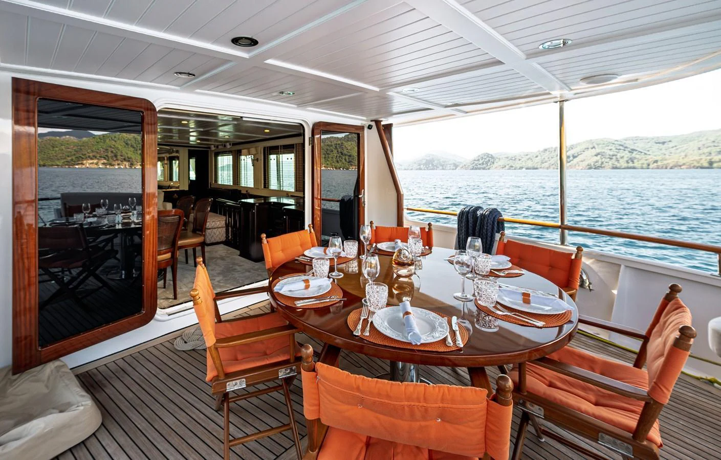 The aft deck features an elegant dining area with a round table set for a meal, offering stunning views of the surrounding waters. aboard LADY L Yacht for Sale