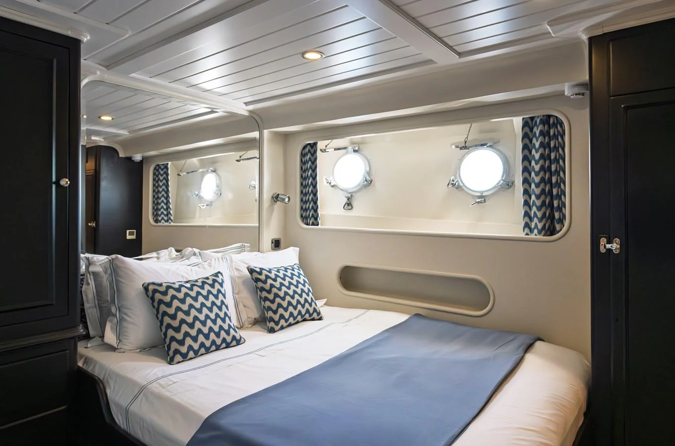 A cozy stateroom featuring a comfortable bed with stylish pillows and porthole windows. aboard LADY L Yacht for Sale
