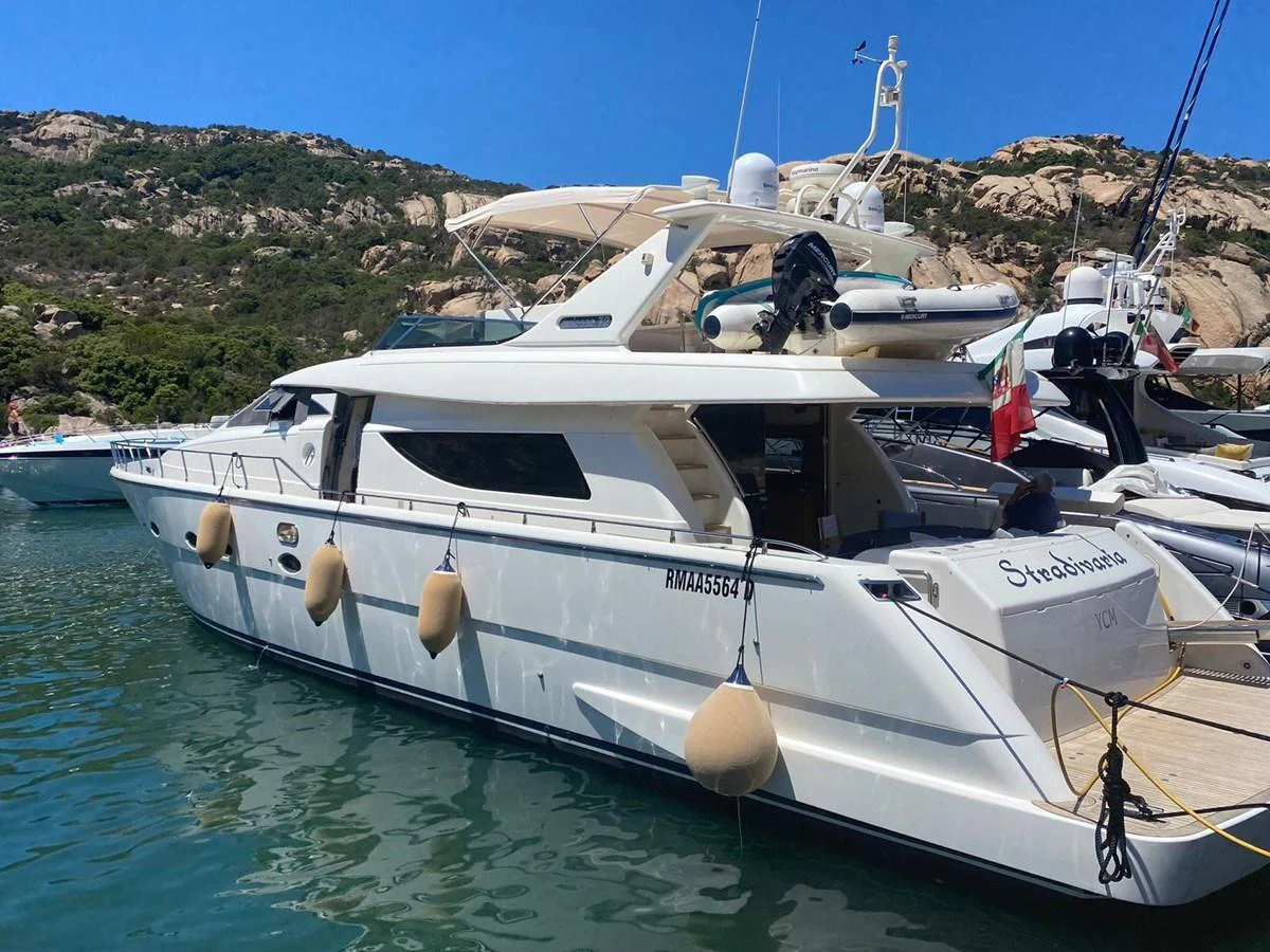 A sleek yacht is moored in a scenic harbor with rocky hills in the background. aboard STRADIVARIA Yacht for Sale