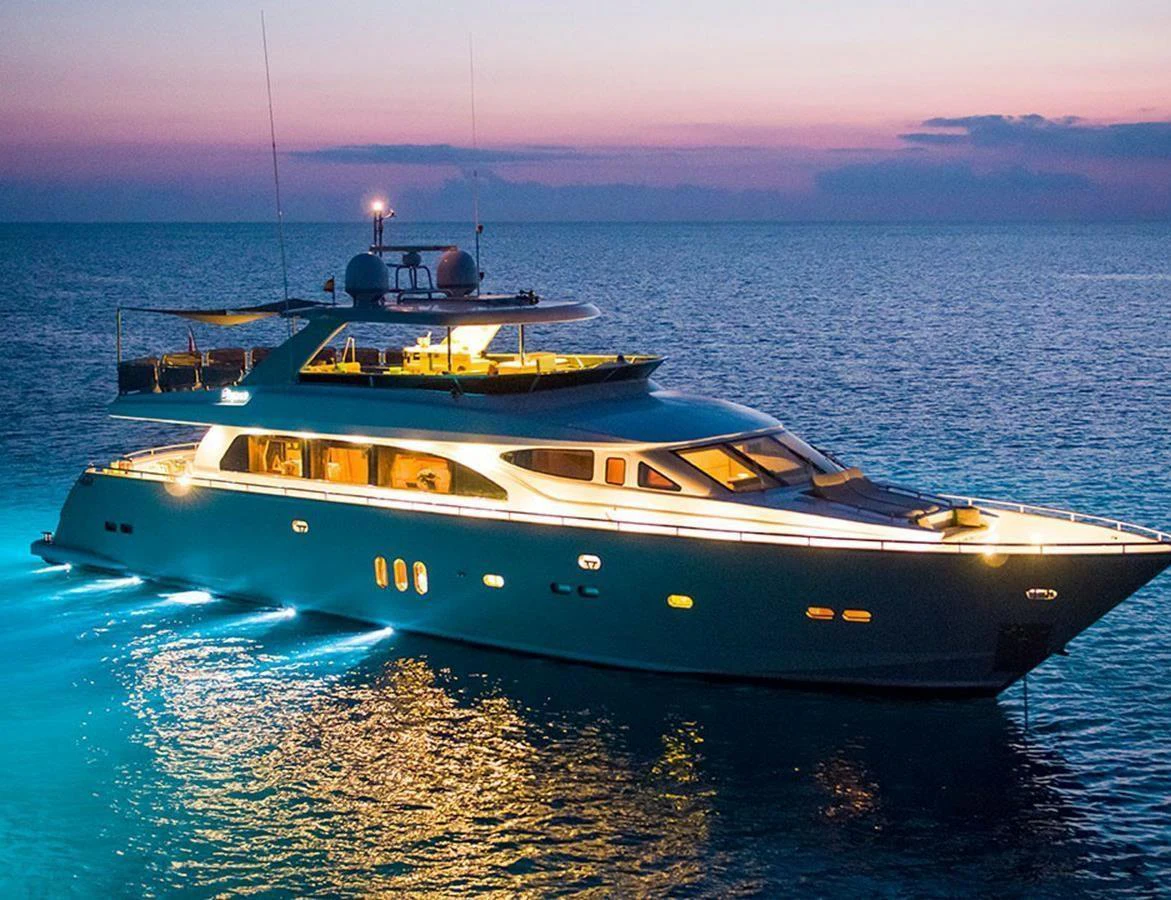 A luxurious yacht is beautifully illuminated at dusk, cruising on calm waters. aboard MR & MRS SMITH Yacht for Sale