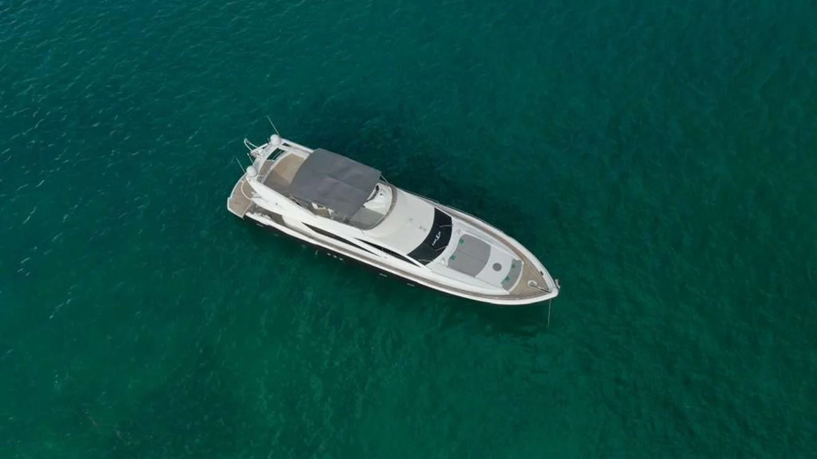 A sleek yacht floats gracefully on clear, turquoise waters, showcasing its elegant design from an aerial perspective. aboard 2006 SUNSEEKER MANHATTAN 'FINS UP' Yacht for Sale