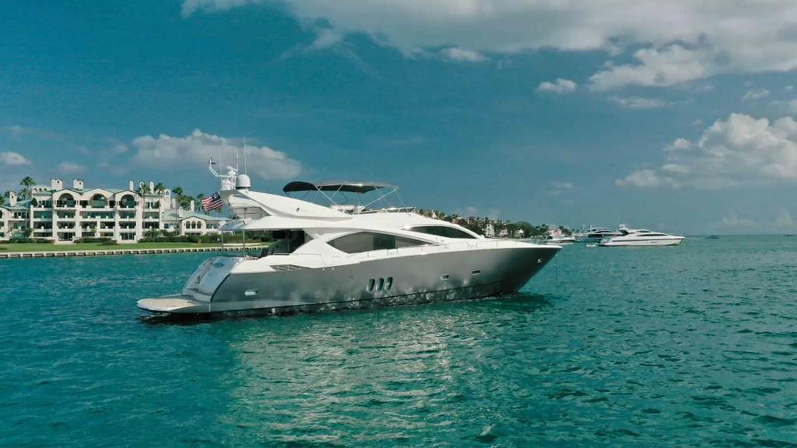 A sleek yacht cruises through calm, turquoise waters with a picturesque shoreline in the background. aboard 2006 SUNSEEKER MANHATTAN 'FINS UP' Yacht for Sale