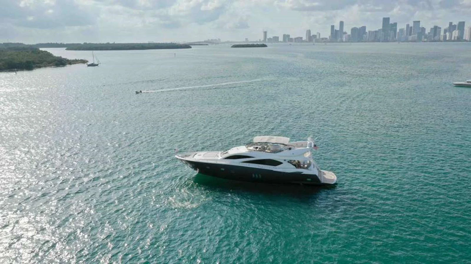 A sleek yacht cruises through calm waters with a cityscape in the background. aboard 2006 SUNSEEKER MANHATTAN 'FINS UP' Yacht for Sale