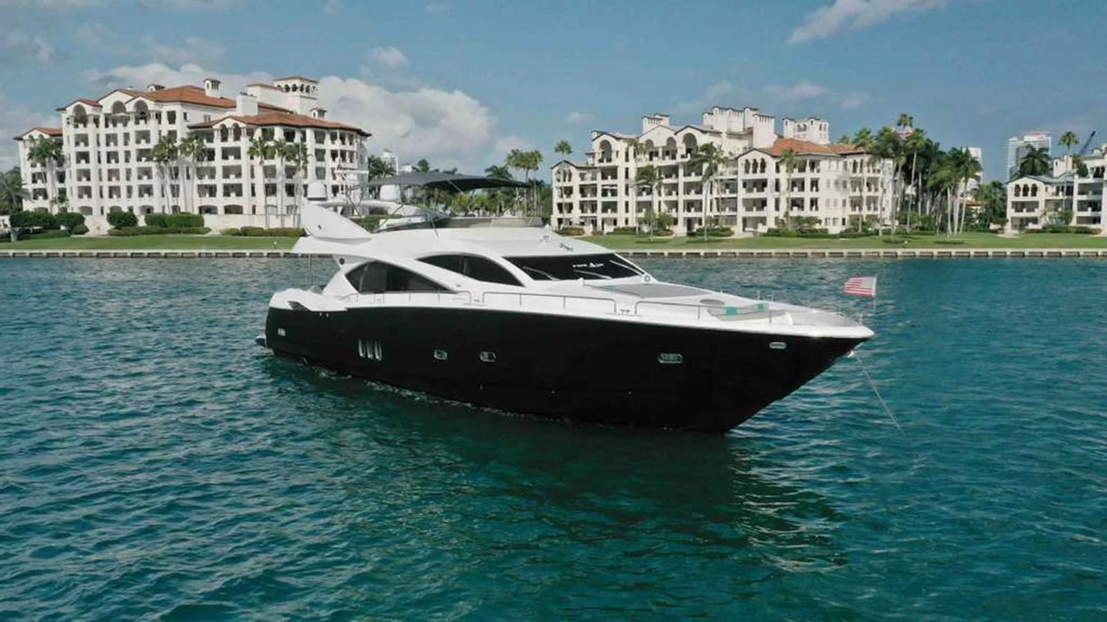 A sleek yacht cruises gracefully on calm waters with a scenic backdrop of luxurious waterfront residences. aboard 2006 SUNSEEKER MANHATTAN 'FINS UP' Yacht for Sale