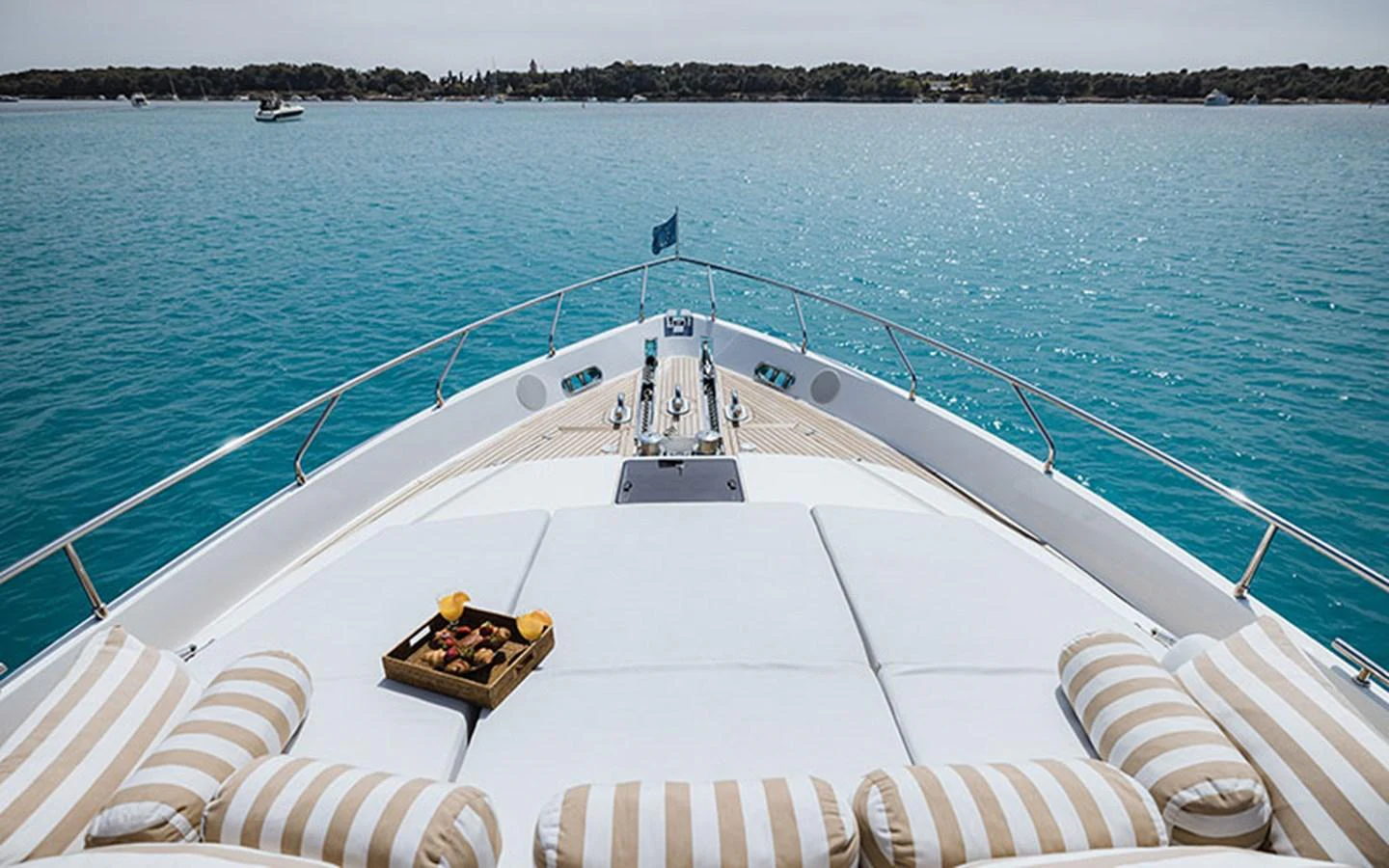 The foredeck offers a luxurious sunbathing area with plush cushions and a tray of refreshments, overlooking serene blue waters. aboard ONYX Yacht for Sale
