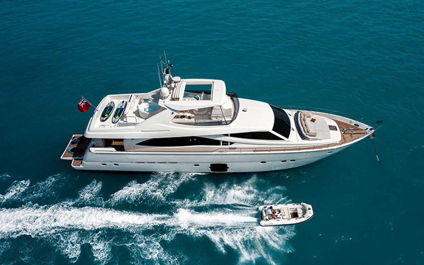A sleek white yacht cruises through clear blue waters, accompanied by a small tender. aboard ONYX Yacht for Sale