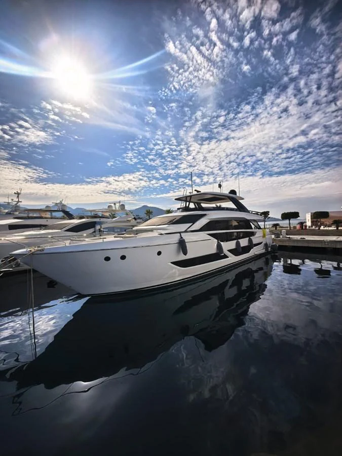 A sleek yacht is docked at a marina under a partly cloudy sky with the sun shining brightly. aboard TBN 860 Yacht for Sale