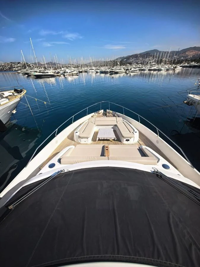The yacht's bow offers a luxurious sunbathing area with plush cushions, set against a serene marina backdrop. aboard TBN 860 Yacht for Sale