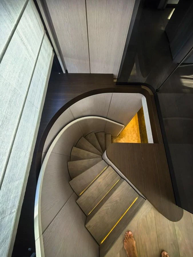 A modern, curved staircase with wooden steps and subtle lighting leads to the lower deck. aboard TBN 860 Yacht for Sale