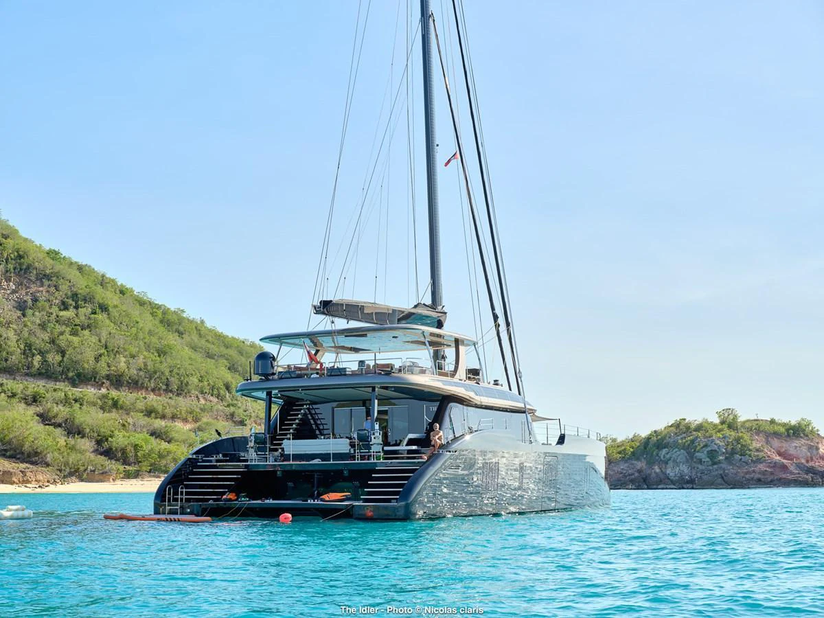 A sleek and modern yacht is anchored in a serene bay with lush greenery in the background. aboard THE IDLER Yacht for Sale
