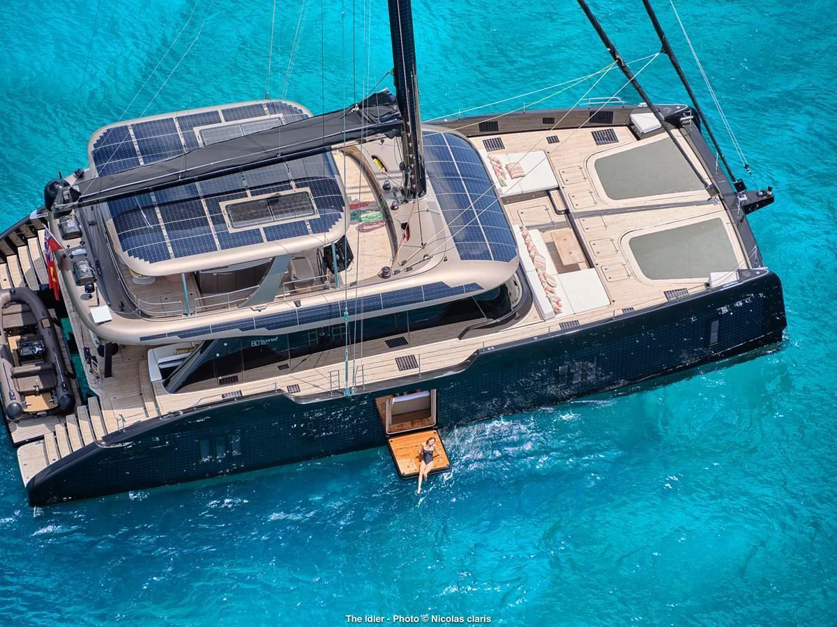 A luxurious catamaran with solar panels on the deck, anchored in crystal-clear turquoise waters. aboard THE IDLER Yacht for Sale