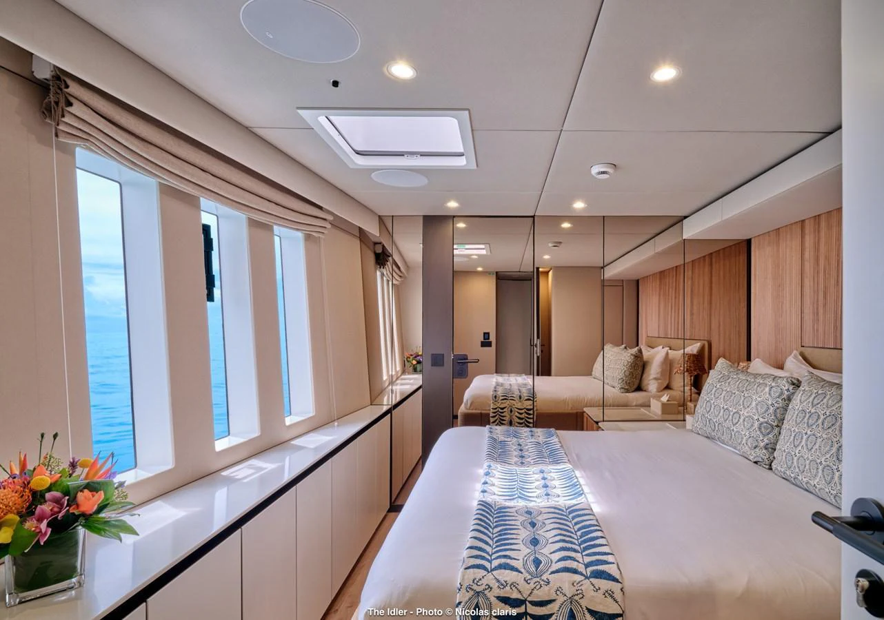 The guest stateroom offers a serene and inviting space with large windows and elegant decor. aboard THE IDLER Yacht for Sale