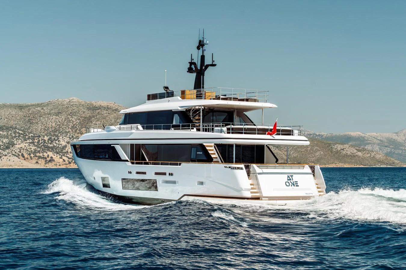A sleek and modern yacht cruising on clear blue waters with a scenic coastline in the background. aboard AT ONE Yacht for Sale