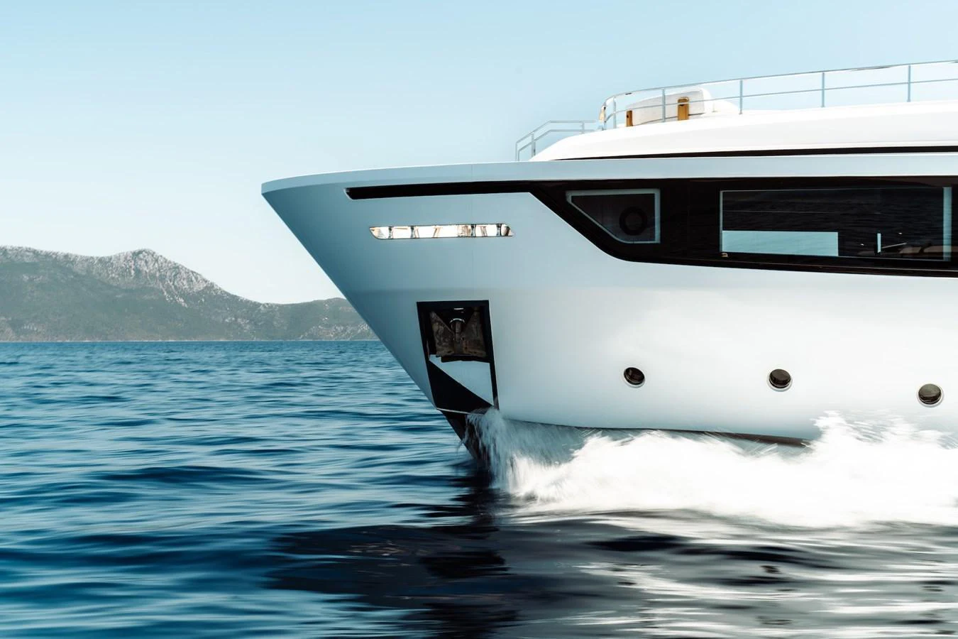 A sleek yacht cuts through the water with a stunning backdrop of mountains. aboard AT ONE Yacht for Sale