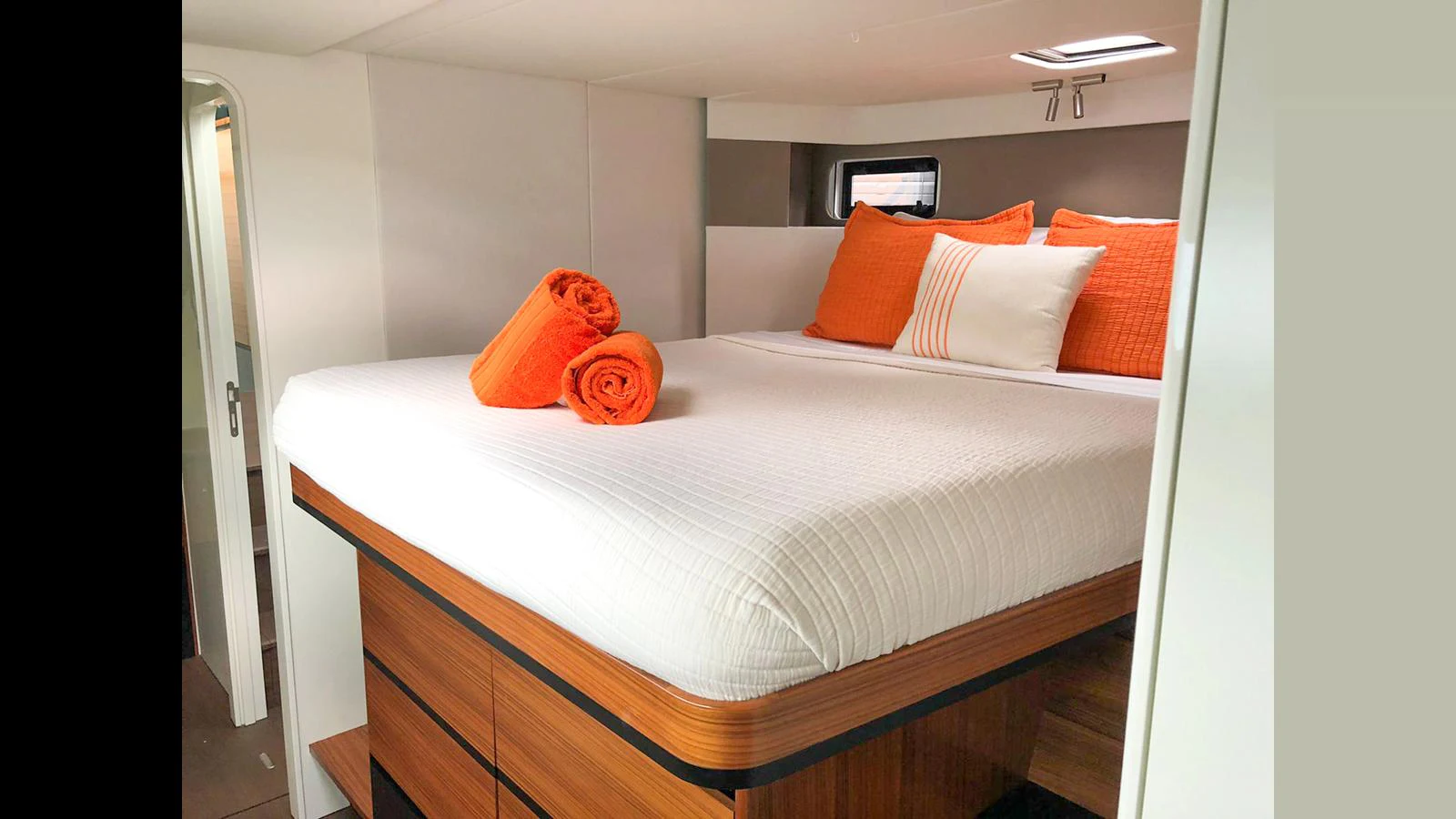 The stateroom features a cozy bed adorned with vibrant orange accents and neatly folded towels. aboard GUNBOAT 80 Yacht for Sale
