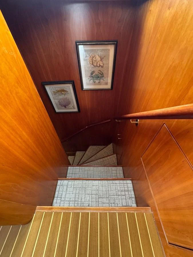 A beautifully crafted wooden staircase leads to the lower deck, adorned with framed artwork. aboard 68' HARGRAVE OPEN BRIDGE Yacht for Sale