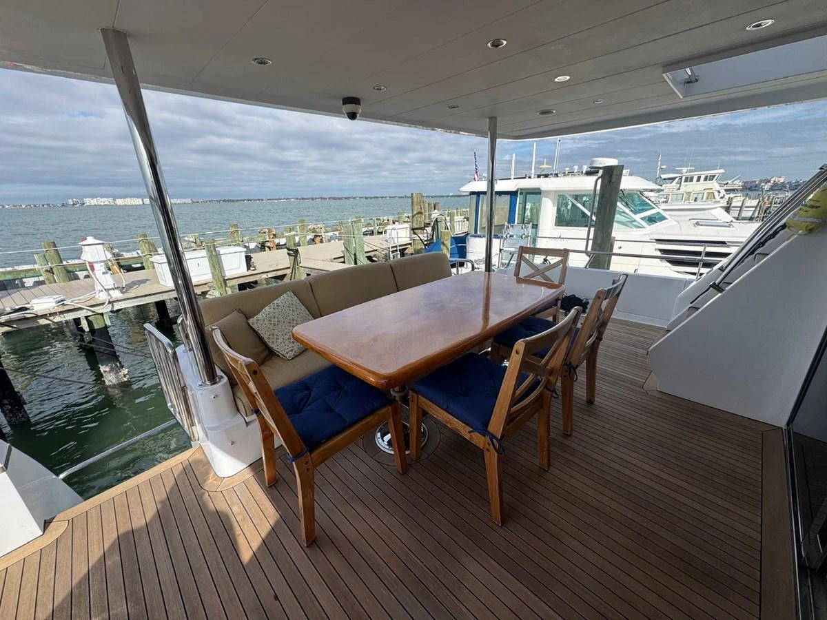 The aft deck features a spacious dining area with a wooden table and comfortable seating, perfect for alfresco meals with a view of the marina. aboard 68' HARGRAVE OPEN BRIDGE Yacht for Sale