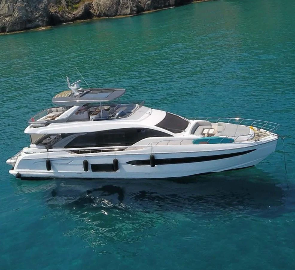A sleek and modern yacht floats gracefully on clear blue waters near a rocky shoreline. aboard KOKO Yacht for Sale