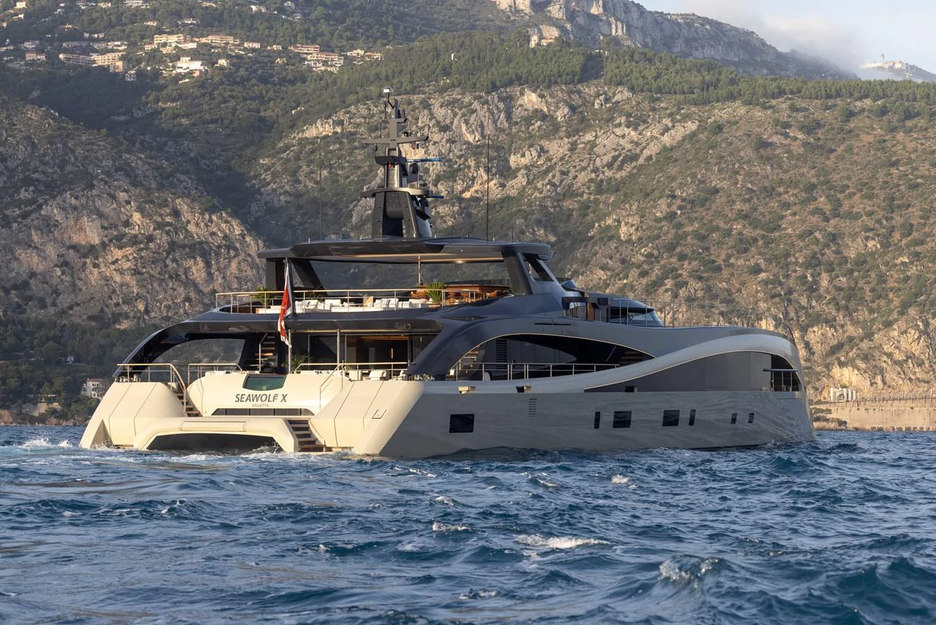A sleek yacht cruises along a scenic coastline with mountainous terrain in the background. aboard SEAWOLF X Yacht for Sale