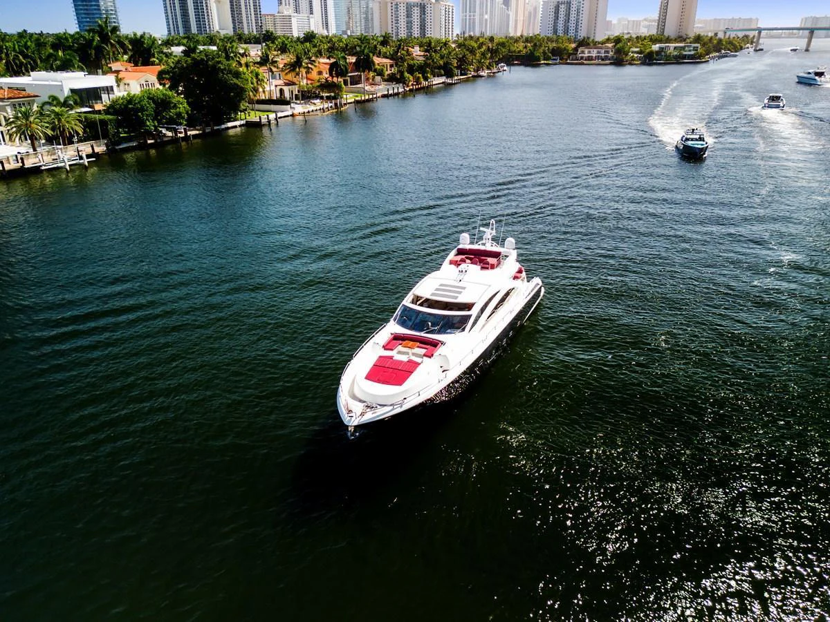 A sleek yacht cruises through a scenic waterway with a vibrant cityscape in the background. aboard GBXSK84PRD13 Yacht for Sale