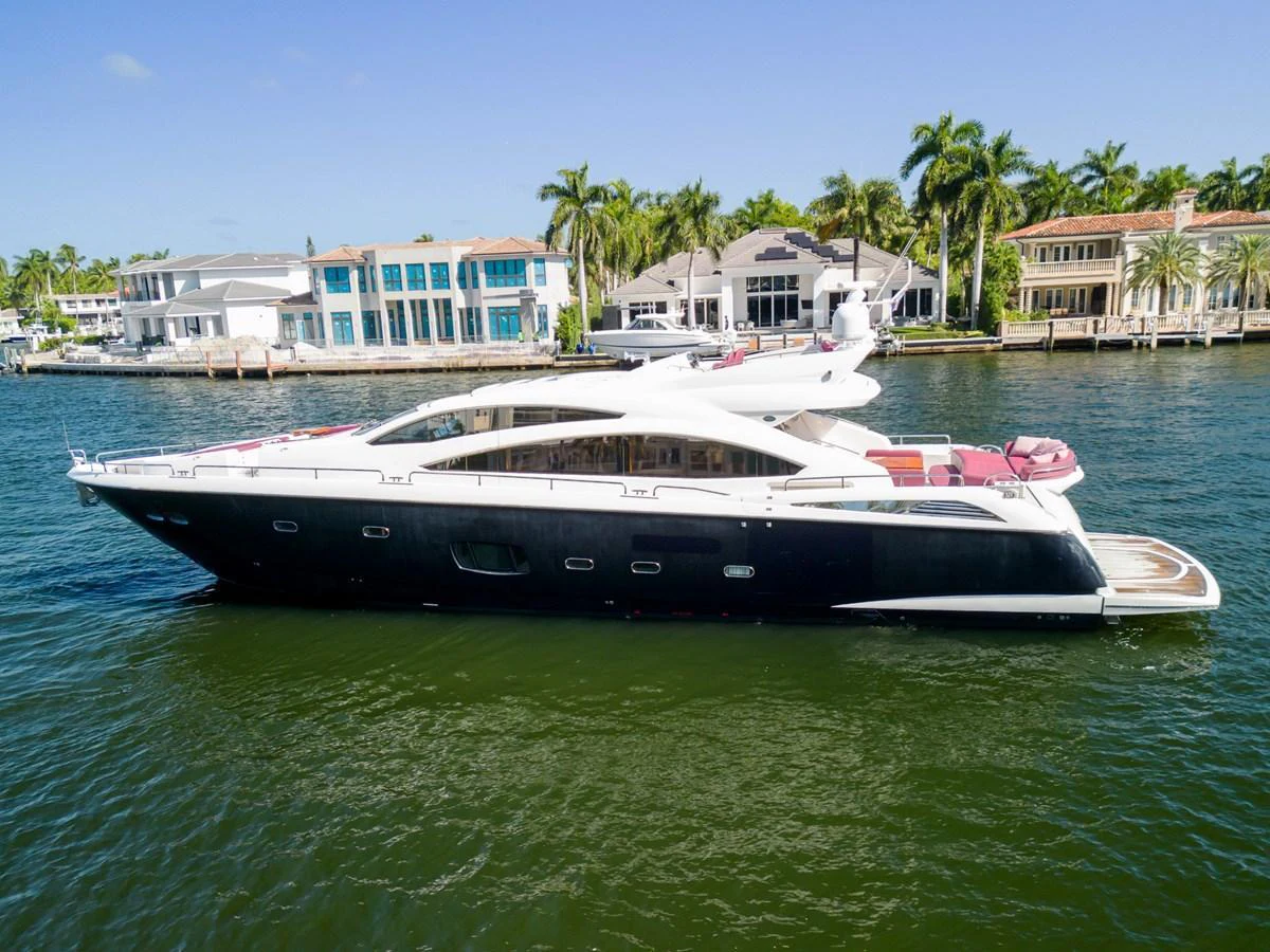 A sleek and modern yacht cruising along a waterfront lined with luxurious homes. aboard GBXSK84PRD13 Yacht for Sale