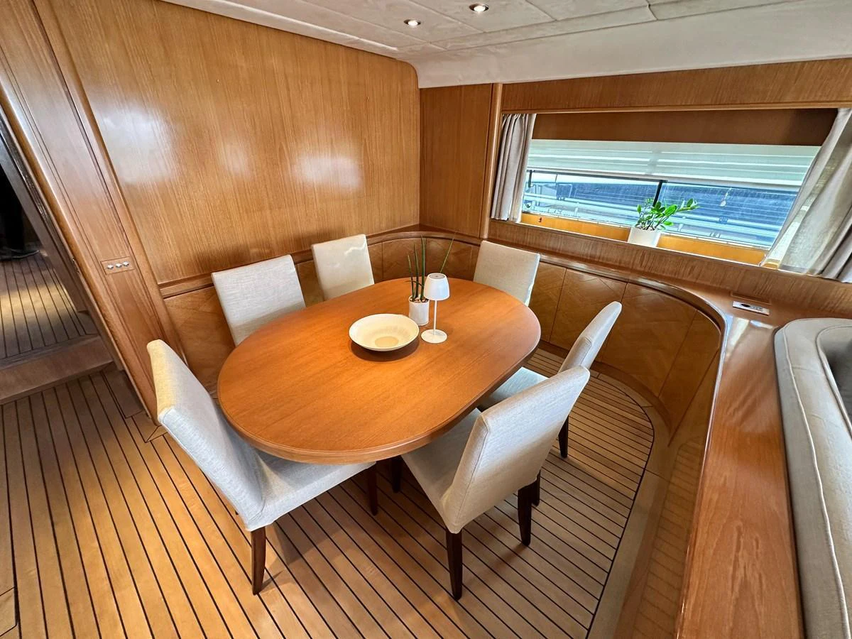 The yacht's dining area features a polished wooden table surrounded by comfortable upholstered chairs, set against a backdrop of sleek wood paneling and large windows. aboard GALINI Yacht for Sale