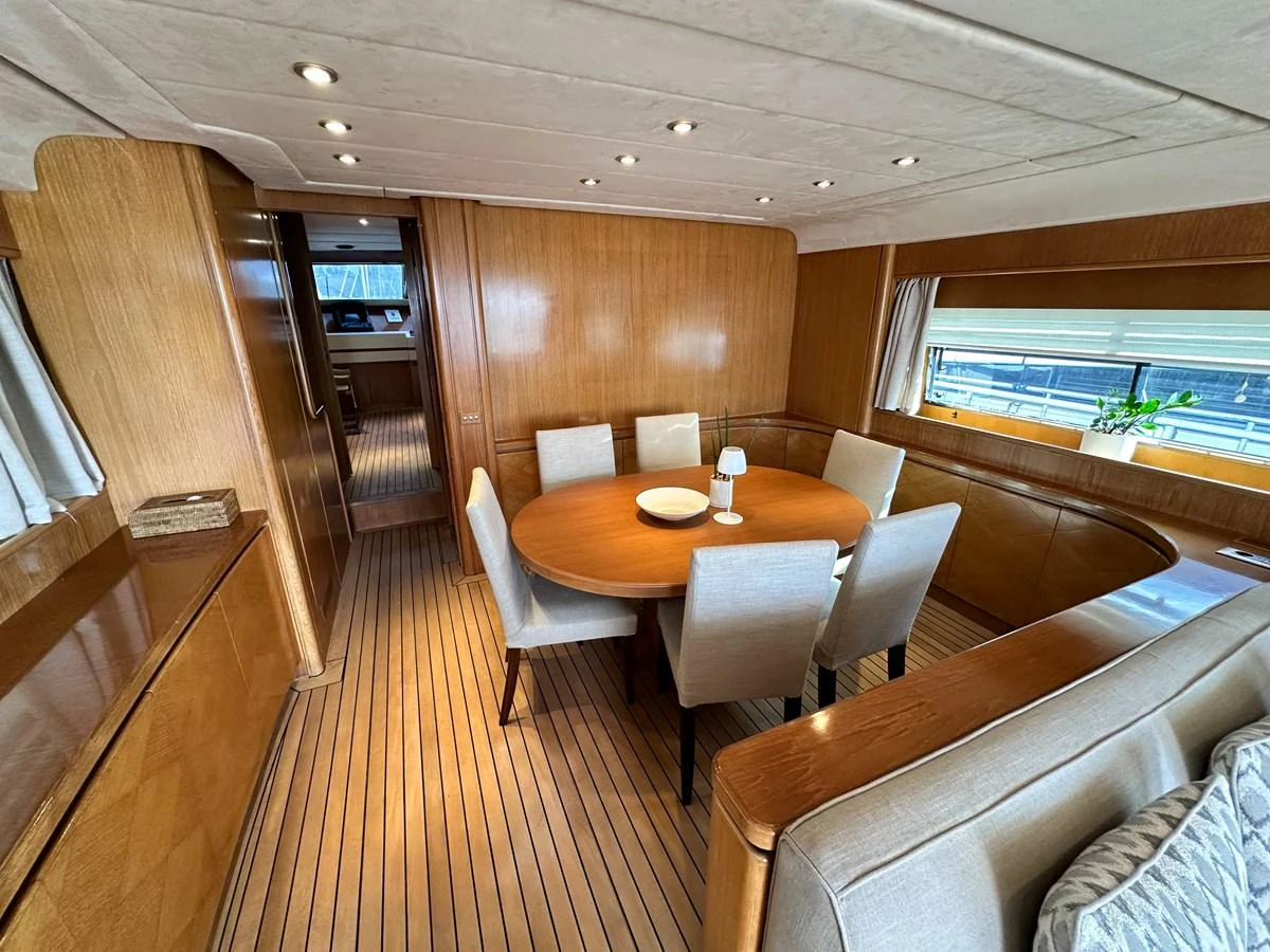 The yacht's dining area features a round wooden table surrounded by comfortable chairs, set in a warmly lit, wood-paneled room. aboard GALINI Yacht for Sale