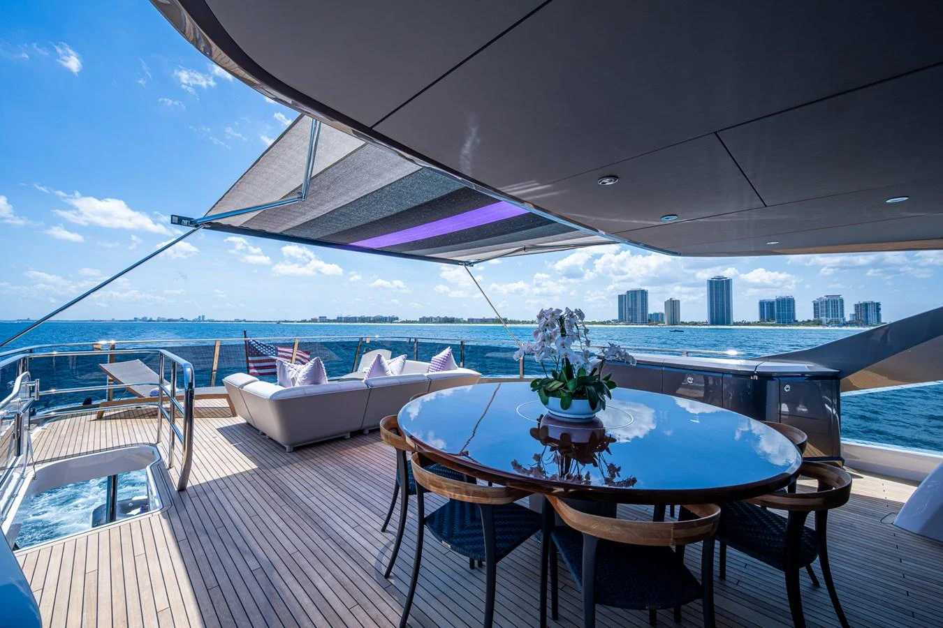 a table on a deck with a view of a city and water aboard SPLASH Yacht for Sale