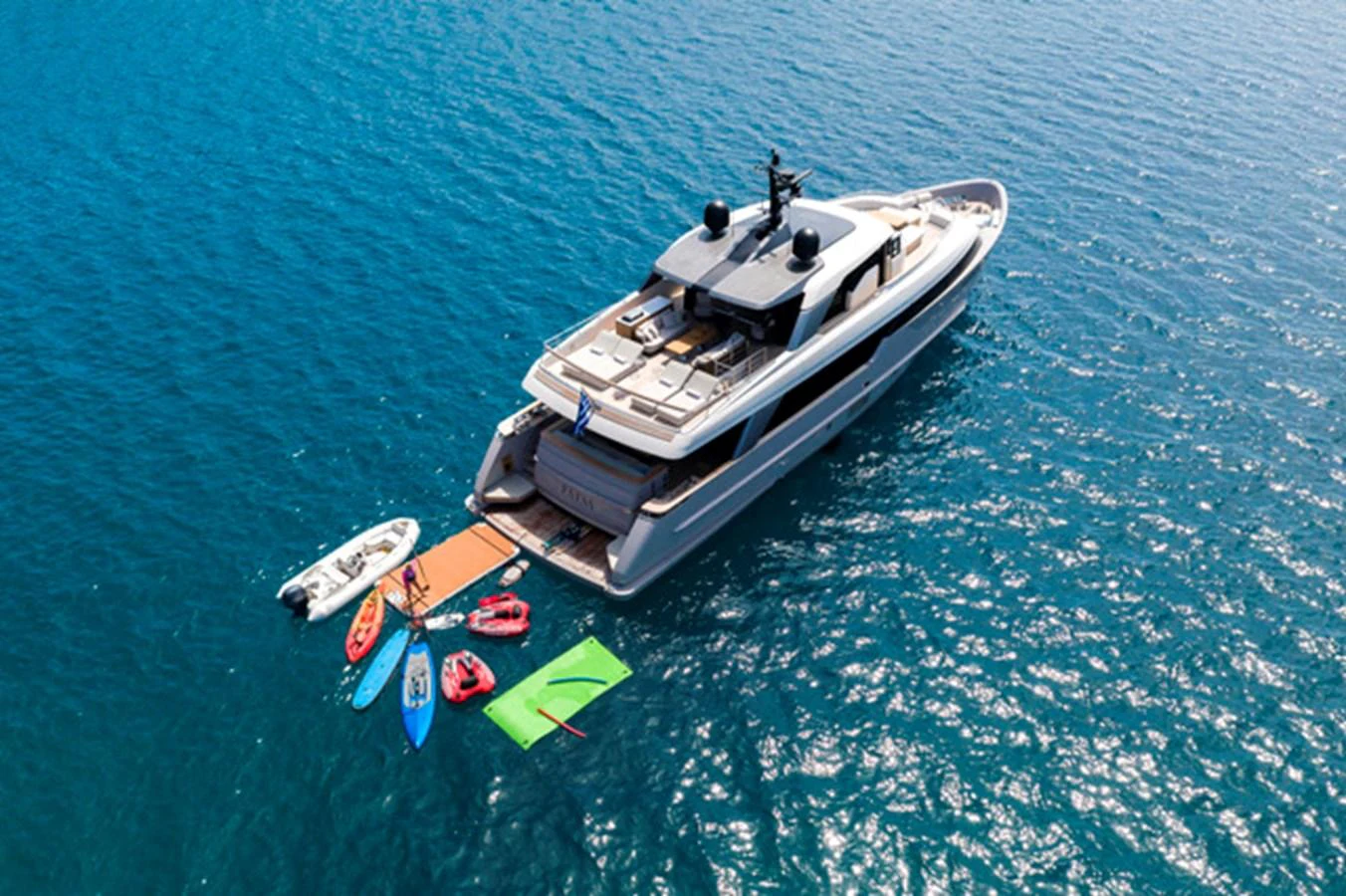 A luxurious yacht is anchored in clear blue waters, with various water toys and a tender floating nearby. aboard FATSA Yacht for Sale
