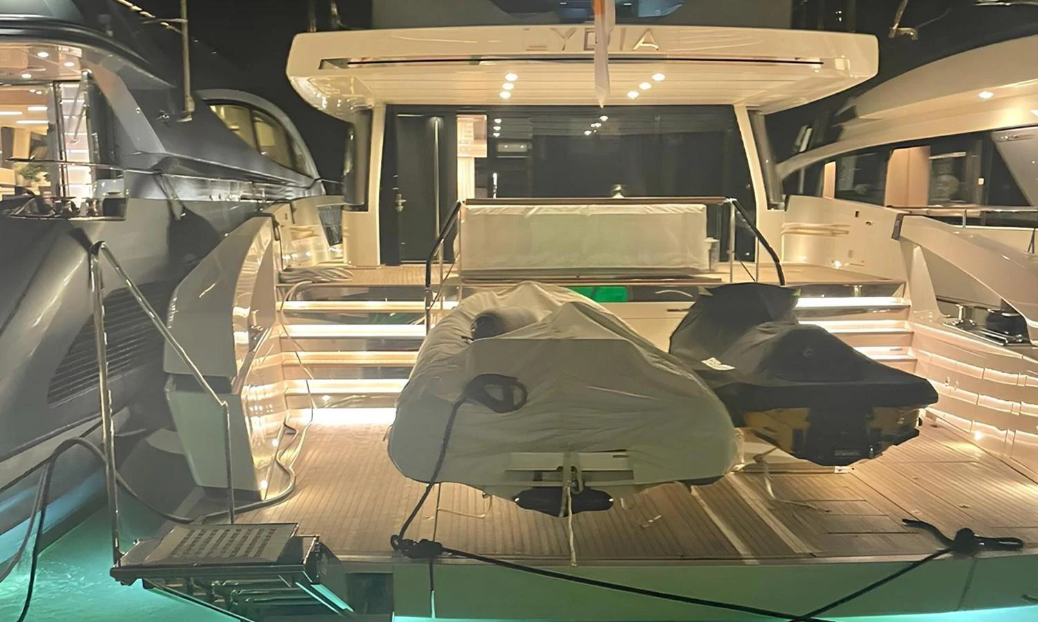 The yacht's aft deck is illuminated beautifully at night, showcasing a tender and a jet ski covered and secured. aboard LYDIA Yacht for Sale