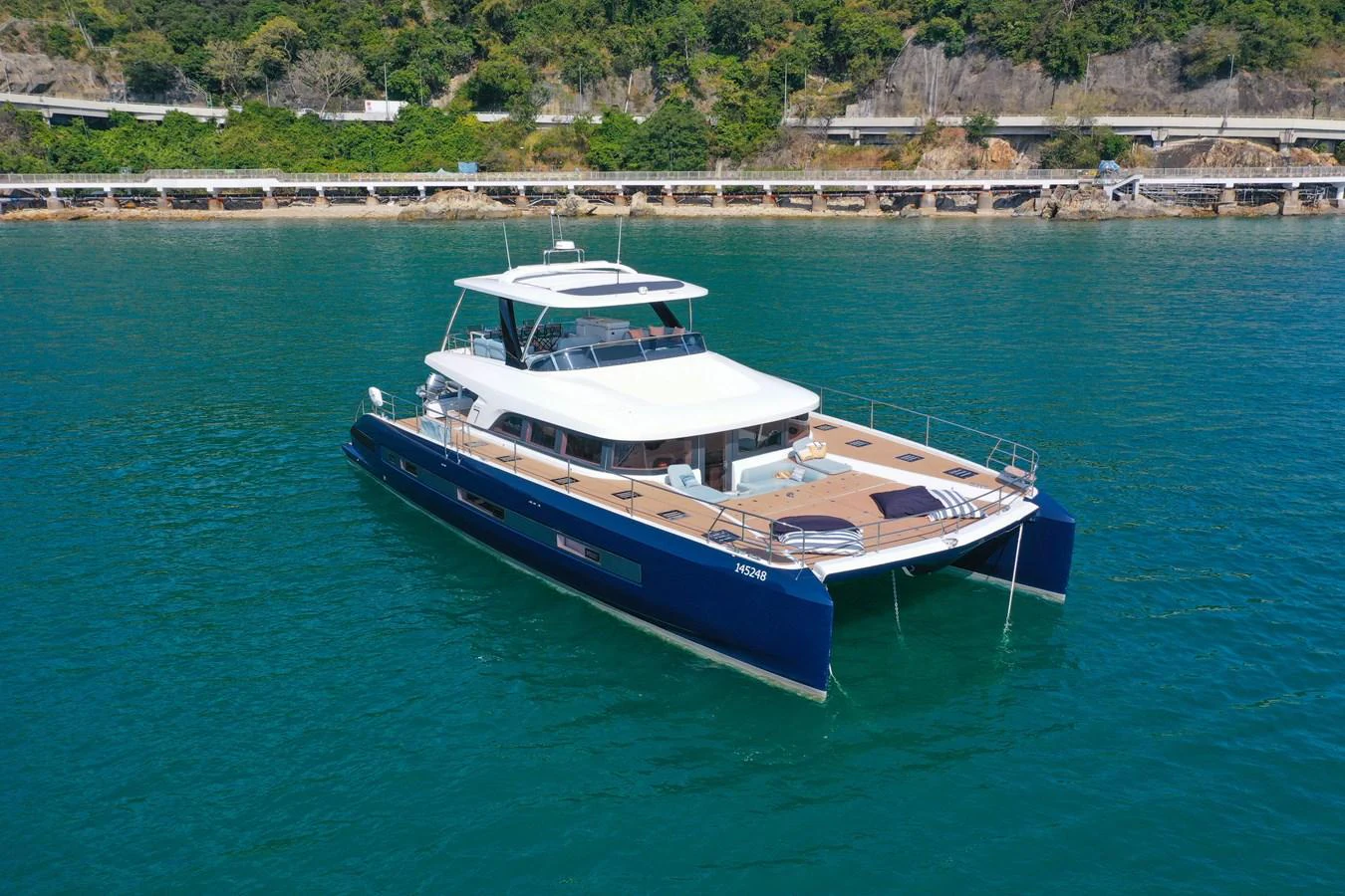 A sleek and modern catamaran yacht cruising on serene waters with lush greenery in the background. aboard LAGOON SIXTY 7 Yacht for Sale