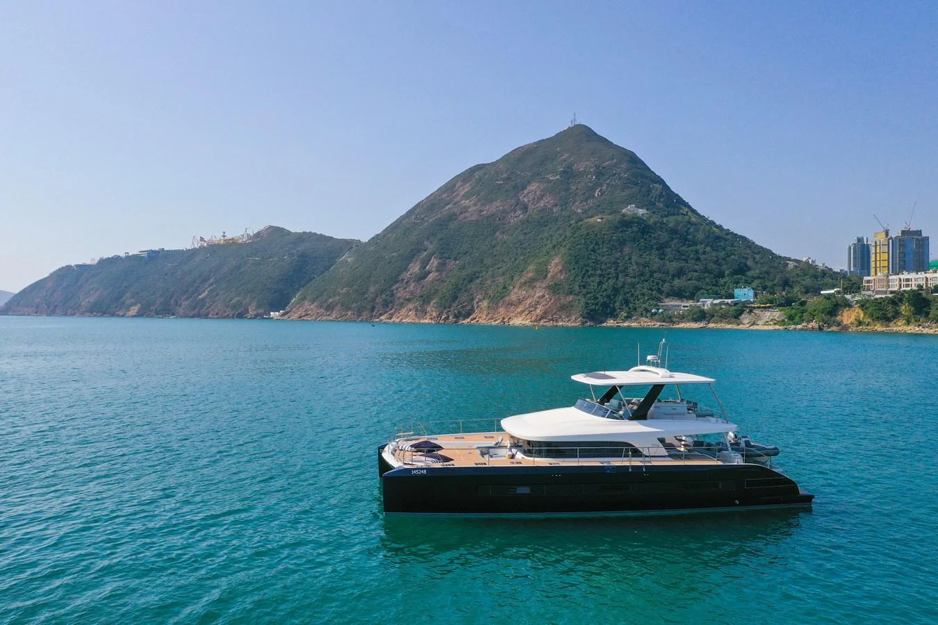 A sleek yacht cruises on calm waters with a scenic mountainous backdrop. aboard LAGOON SIXTY 7 Yacht for Sale