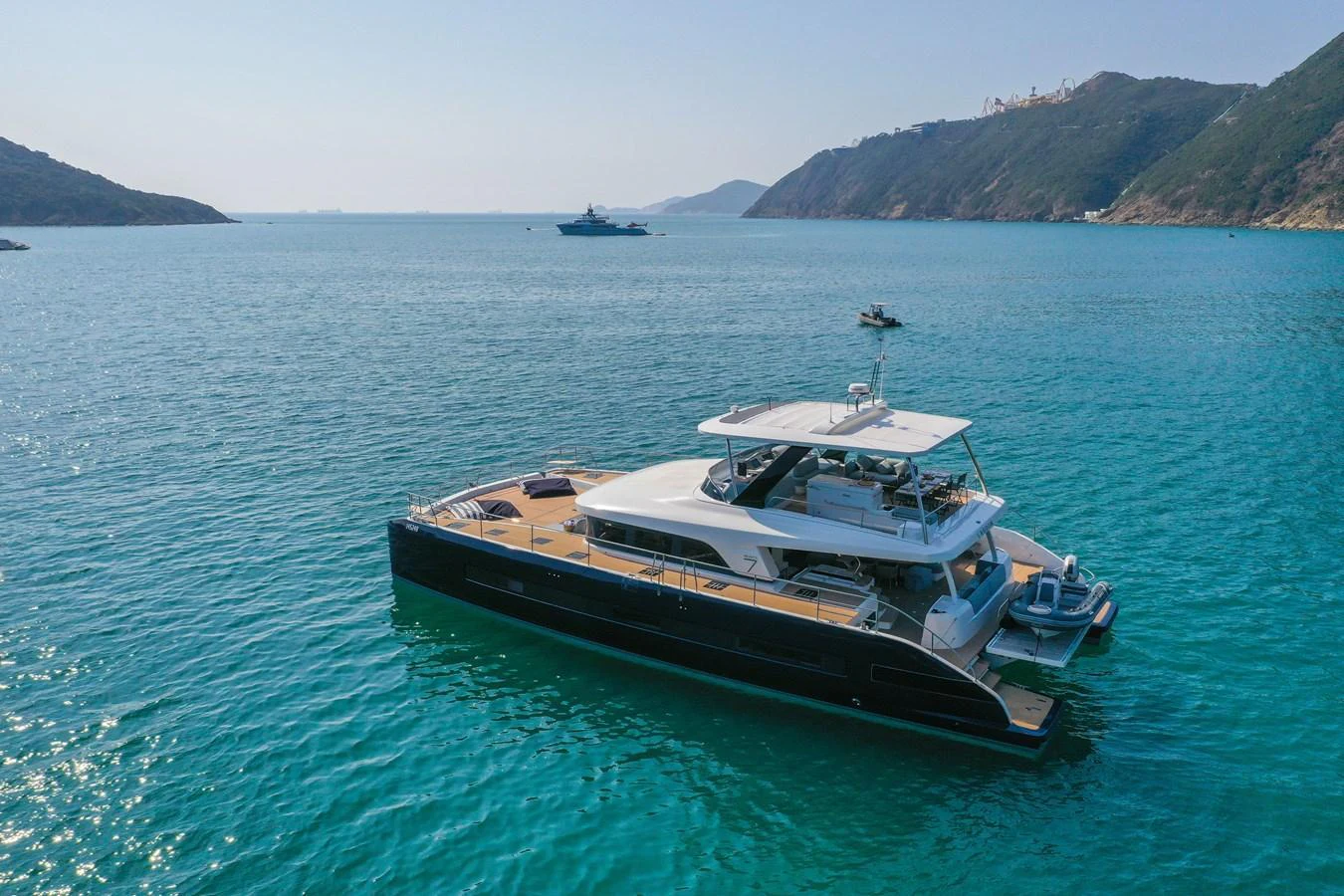 A sleek yacht glides gracefully on tranquil blue waters, surrounded by scenic hills. aboard LAGOON SIXTY 7 Yacht for Sale