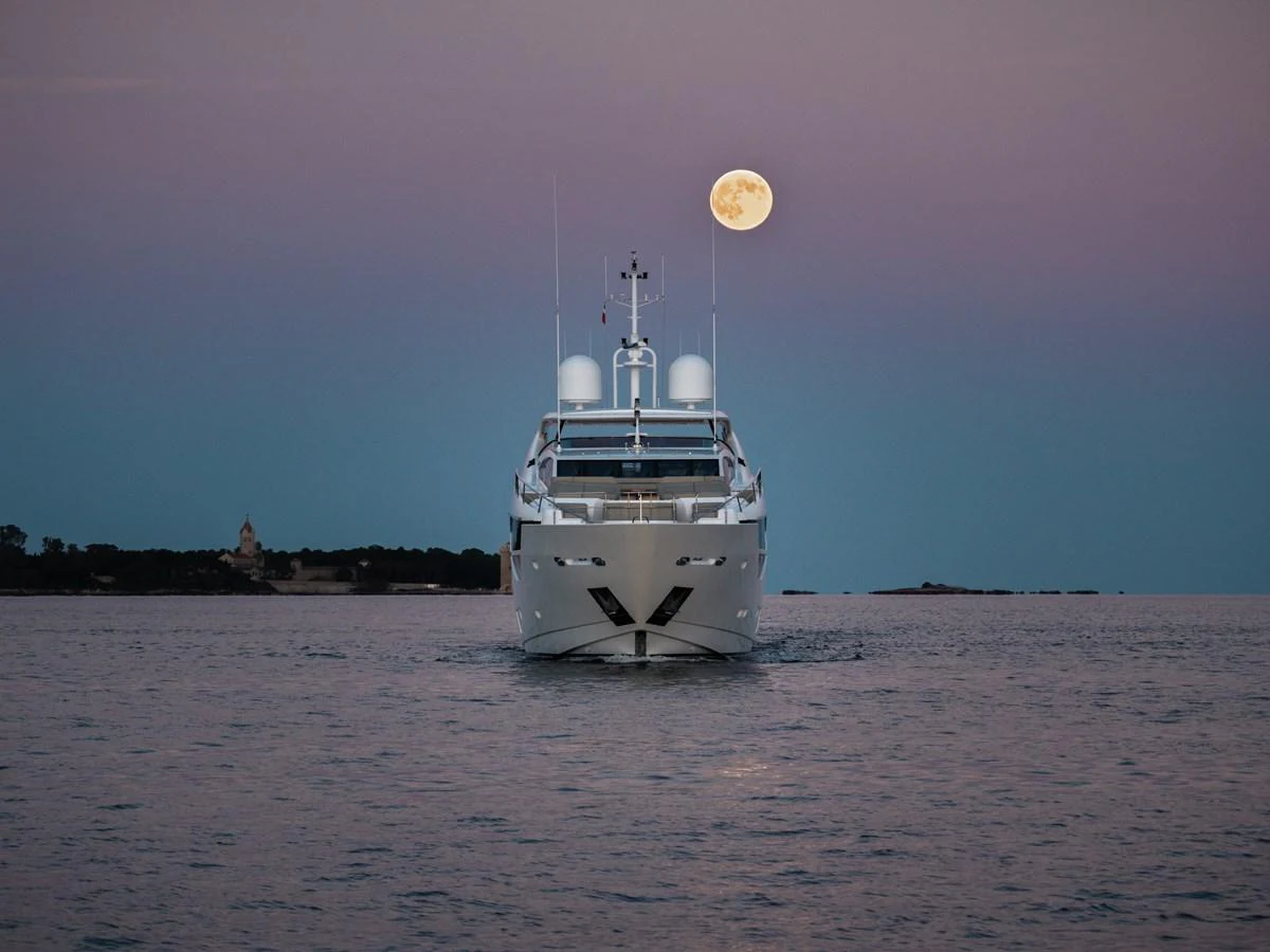 A luxurious yacht is seen head-on, cruising on calm waters under a full moon. aboard KING POWER Yacht for Sale