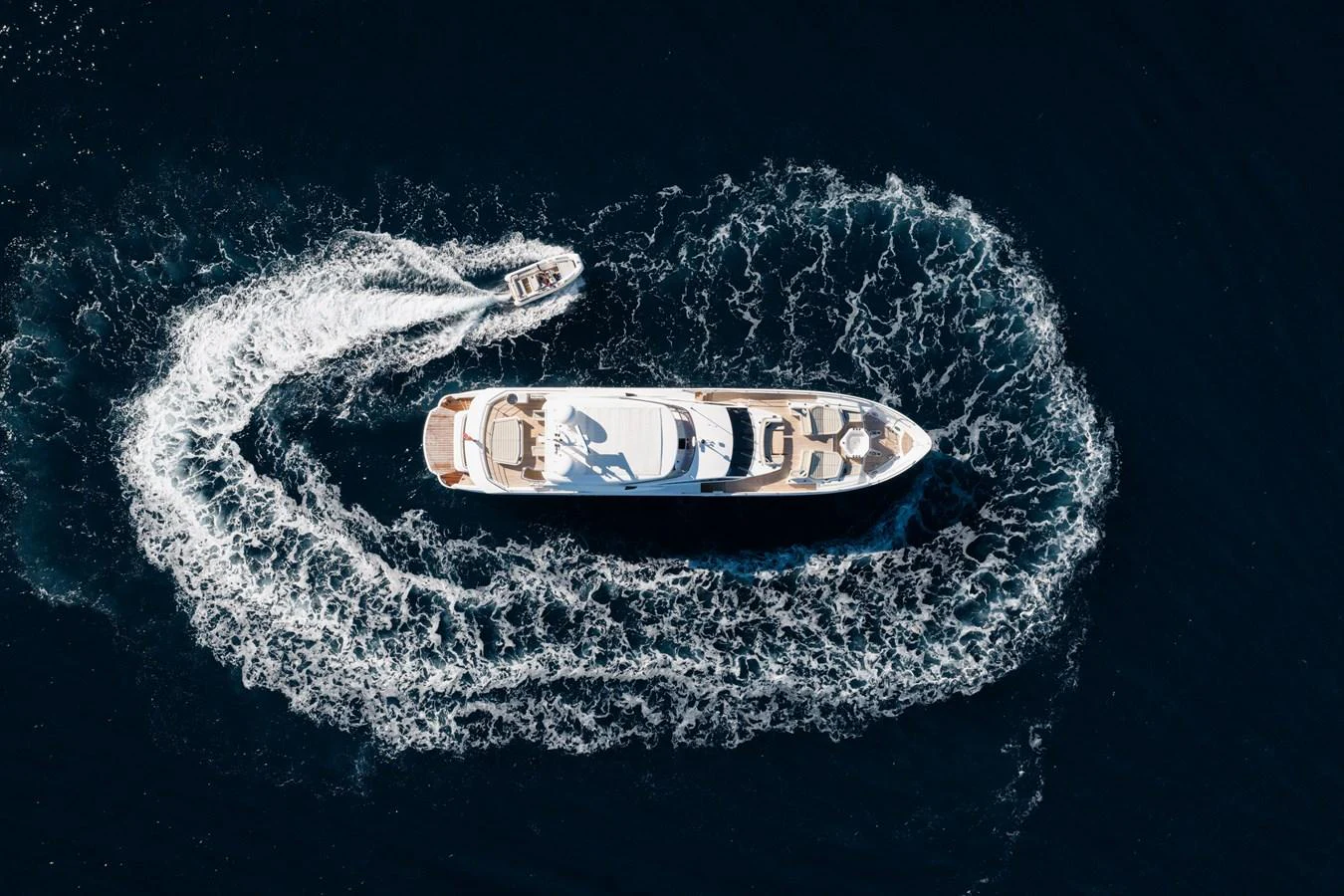An aerial view of a luxurious yacht cruising through the water, accompanied by a tender creating a dynamic wake pattern. aboard KING POWER Yacht for Sale