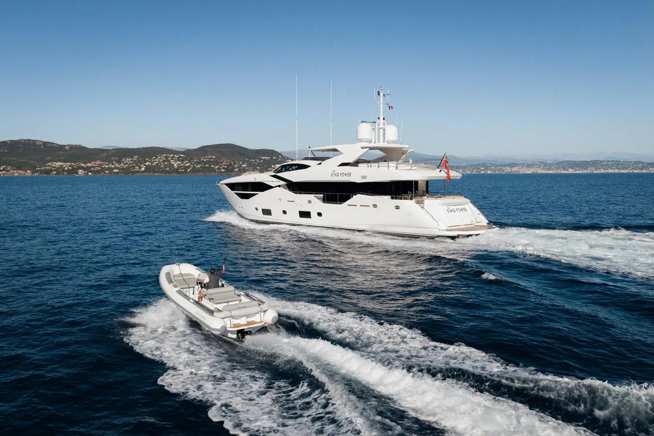 A sleek yacht cruises through the open water accompanied by a tender boat. aboard KING POWER Yacht for Sale