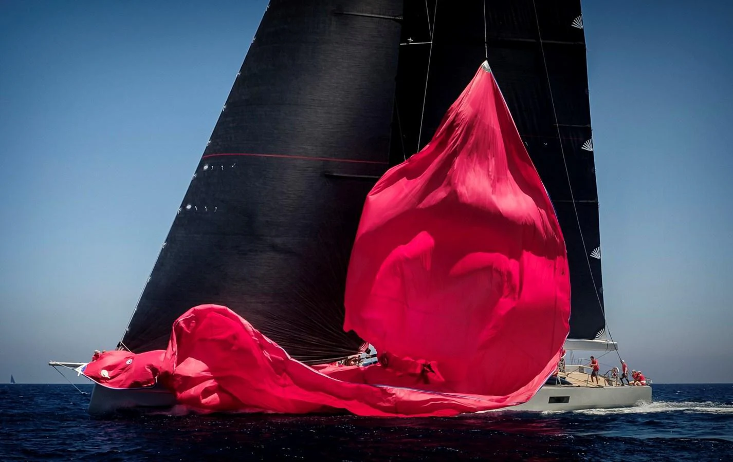 A sleek sailing yacht with a striking red spinnaker billowing in the wind, cutting through the water with elegance. aboard ANOMALY Yacht for Sale
