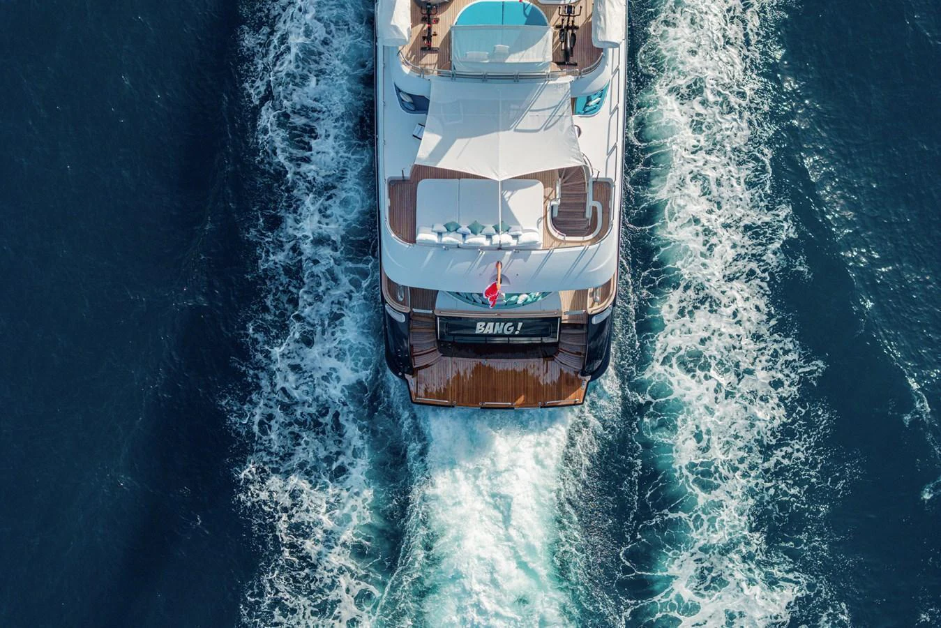 A stunning aerial view of the yacht's aft deck as it cruises through the water, leaving a beautiful wake behind. aboard BANG! Yacht for Sale