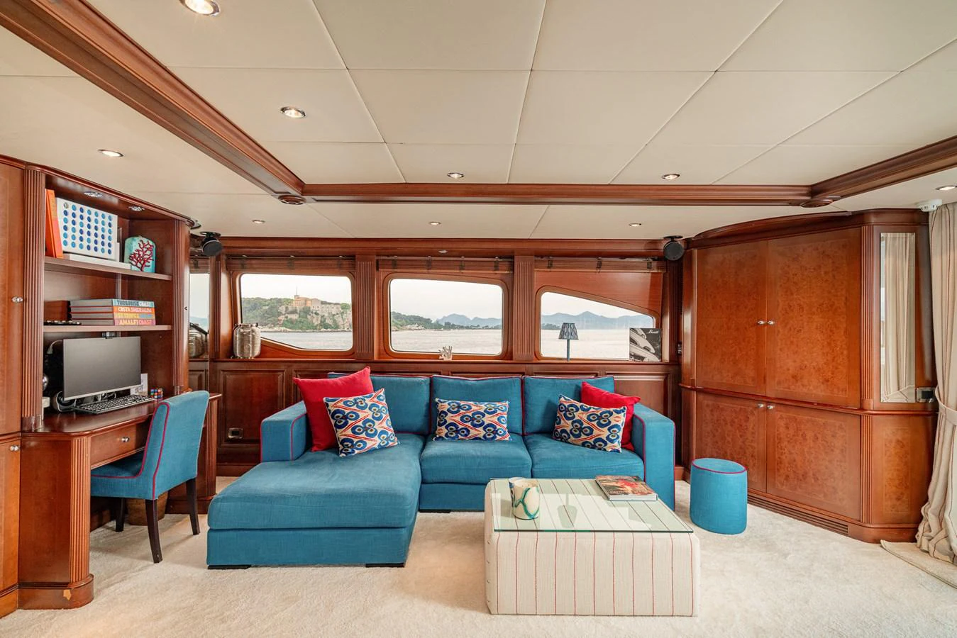 The salon features a comfortable seating area with a vibrant blue sofa and large windows offering scenic views. aboard BANG! Yacht for Sale