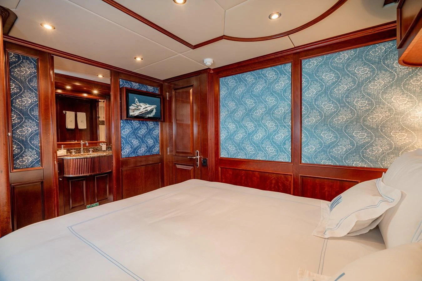 A luxurious stateroom featuring elegant wood paneling and a comfortable bed with a view into the ensuite bathroom. aboard BANG! Yacht for Sale