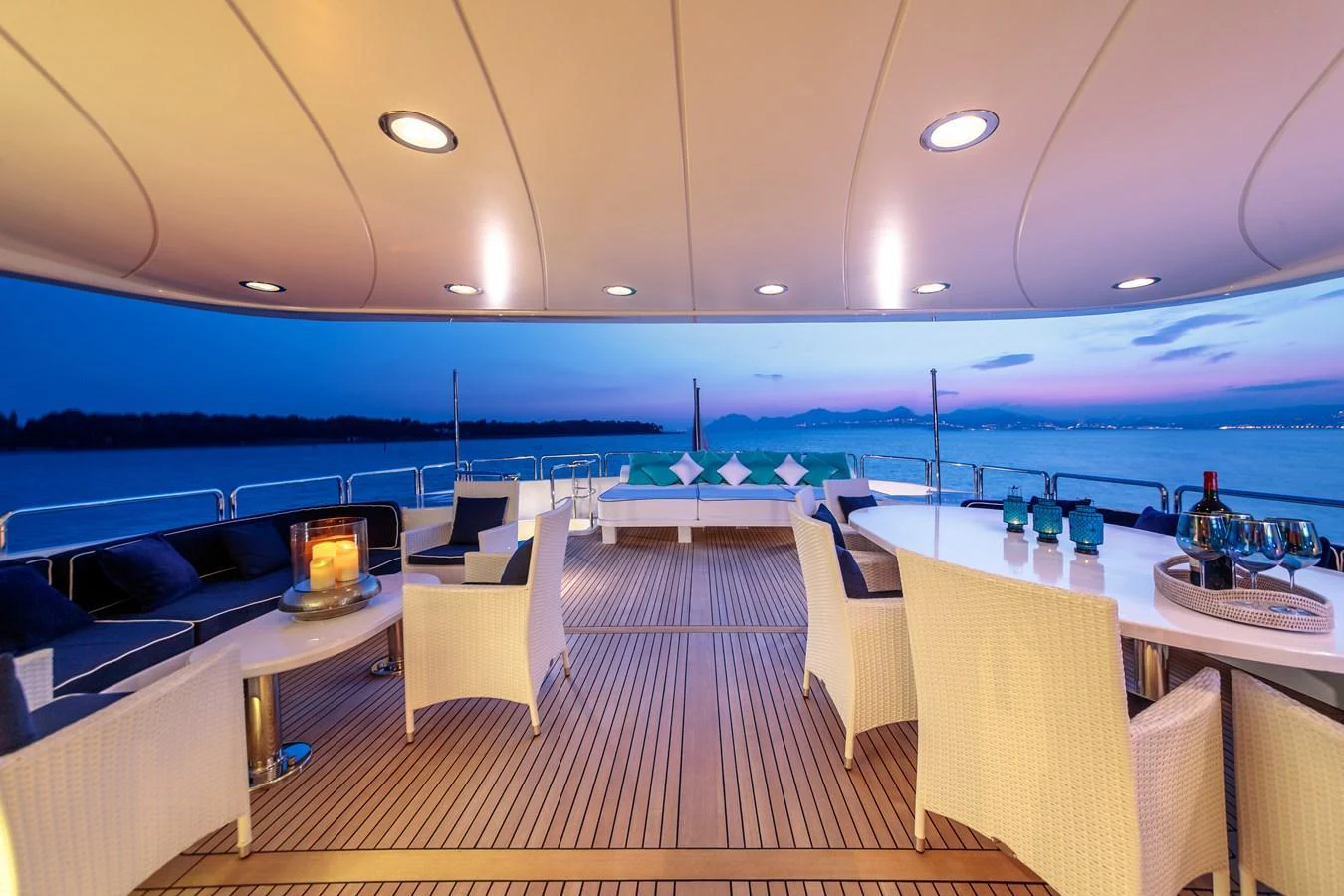 The aft deck offers a luxurious outdoor seating area with a stunning view of the water at dusk. aboard BANG! Yacht for Sale