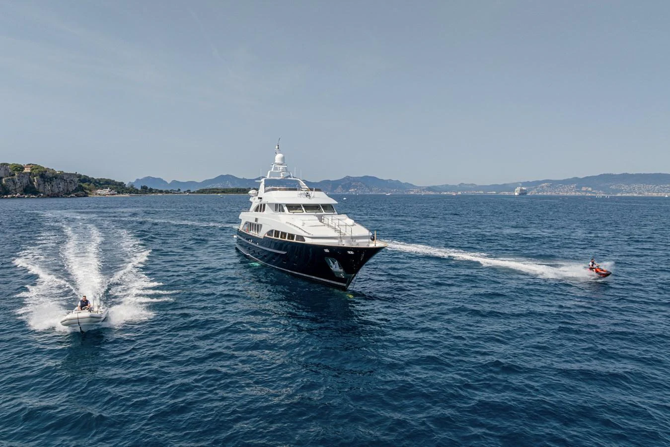 A luxurious yacht cruising on the open sea, accompanied by two smaller watercraft. aboard BANG! Yacht for Sale