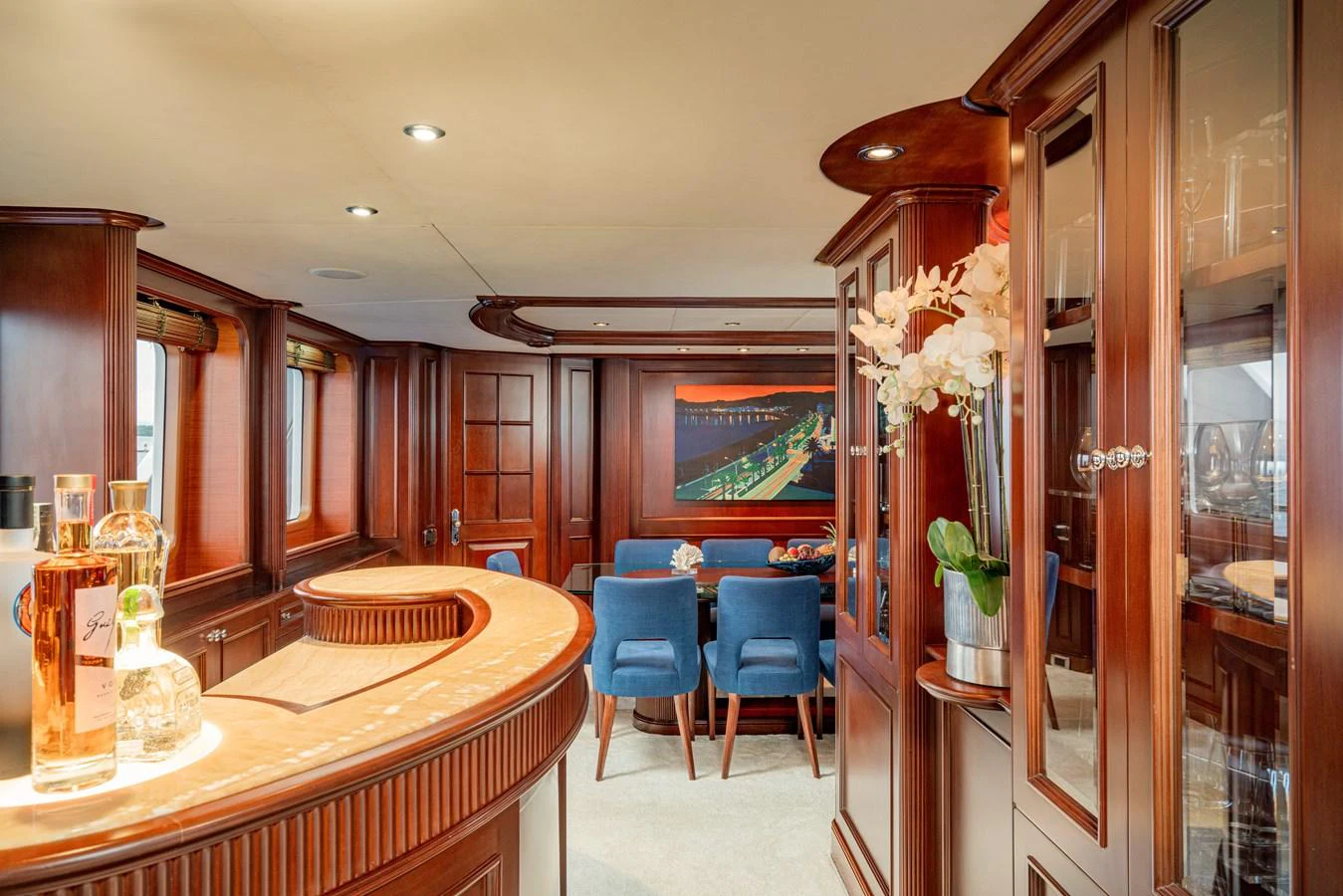 The yacht's salon features elegant wood paneling, a stylish bar, and a cozy dining area with blue chairs. aboard BANG! Yacht for Sale