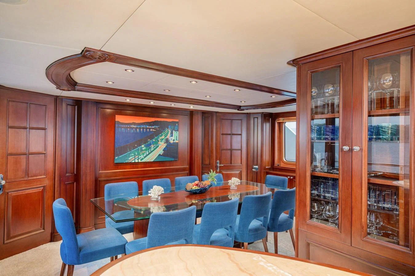 The yacht's dining area features a glass table surrounded by plush blue chairs, complemented by rich wooden cabinetry and elegant decor. aboard BANG! Yacht for Sale