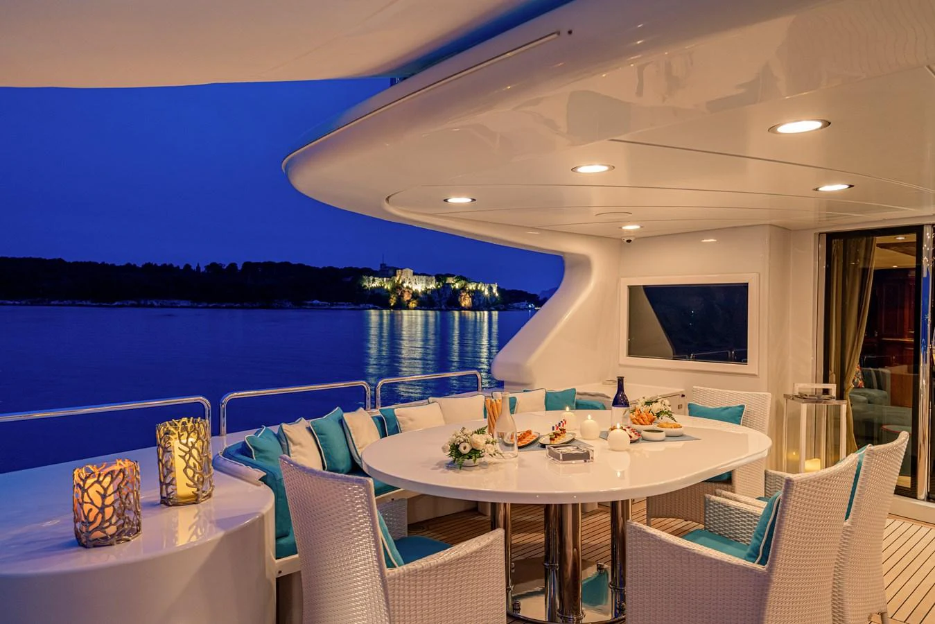 The aft deck features an elegant dining area with a round table, cushioned chairs, and ambient lighting, perfect for evening meals with a view. aboard BANG! Yacht for Sale