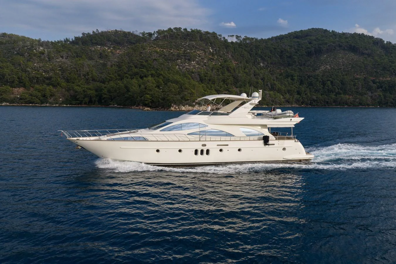 A sleek yacht cruises through calm waters with a scenic forested backdrop. aboard SENIOR S Yacht for Sale