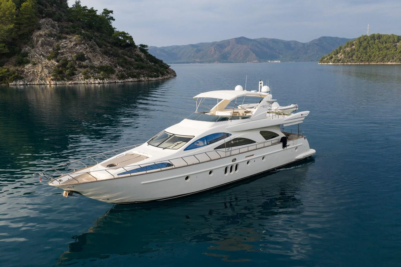 A sleek and elegant yacht glides through calm waters surrounded by scenic, mountainous terrain. aboard SENIOR S Yacht for Sale